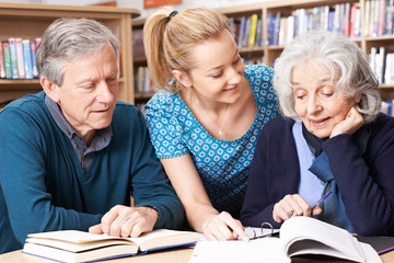 Mature Students Working With Teacher In Library