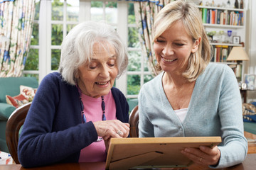 Senior Woman Looks At Photo Frame With Mature Female Neighbor
