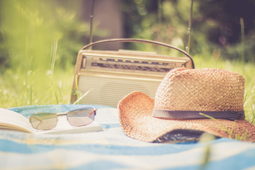 Buch, Strohhut und altes Radio auf Picknickdecke
