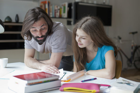 Father assisting daughter in doing homework at table