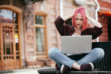young girl with red hair sitting outdoors on a bench with a laptop, bad news
