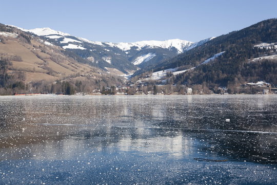 Frozen Zeller See lake with snow capped mountains reflected in ice in alpine resort. Zell am See, Austria