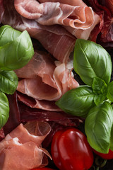 Jambon mix. Ham. Traditional Italian and Spanish salting, smoking, dry-cured dish - jamon Serrano and prosciutto crudo sliced with herbs and tomatos on dark stone background. Copy space. Closeup. 