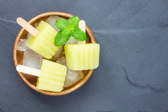 Homemade melon popsicles on grey slate, top view, copy space