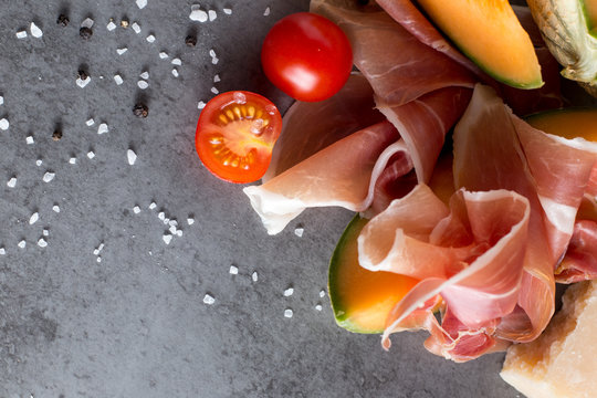 Jambon mix. Ham. Traditional Italian and Spanish salting, smoking, dry-cured dish - jamon Serrano and prosciutto crudo sliced with melon on grey background. Copy space. Closeup.