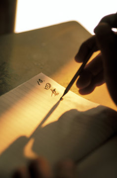 Thailand, Bangkok. Shop owner writes tahi script into notebook at sunset.