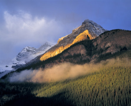 Canada, Alberta, Banff NP. Sunrise strikes the flank of the Canadian Rockies as clouds swirl in Banff NP, a World Heritage Site, Alberta, Canada. 