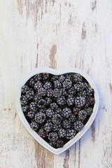 Gefrorene Waldbrombeeren in einer herzförmigen Schüssel auf einem Holztisch