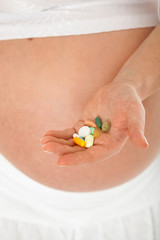 Pregnant young woman with pills in hand, close up
