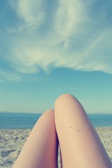Knees of a young woman lying on the beach, on a sunny summer day, with blue sky in the background. Filtered image in faded, retro, Instagram style. Personal pov.