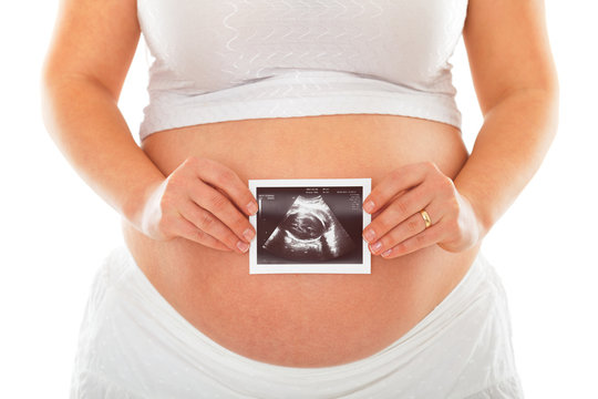 Pregnant woman holding ultrasound scan photo in front of her belly. Isolated on white background. Horizontal shot