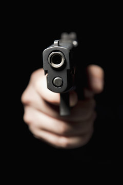 A hand holding a gun and pointing it at the camera, black background