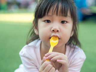 Asian girl child eating a dessert , spoon in her mouth