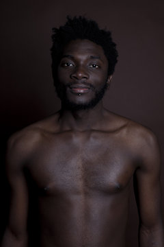 A shirtless hip young man standing against a brown background, waist up