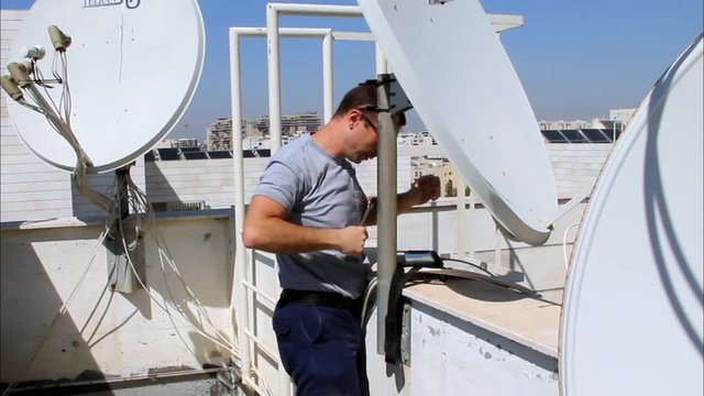 Technician adjusting of a satellite television dish with satellite channels finder,