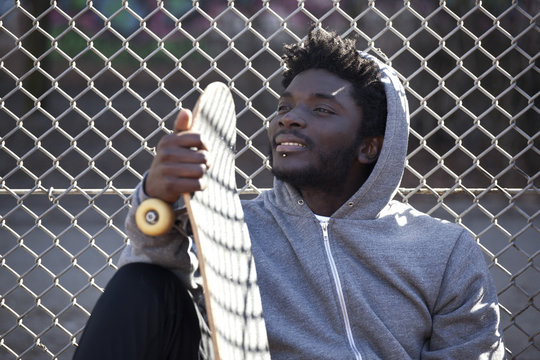 A grinning young man leaning against a chain link fence holding a skateboard