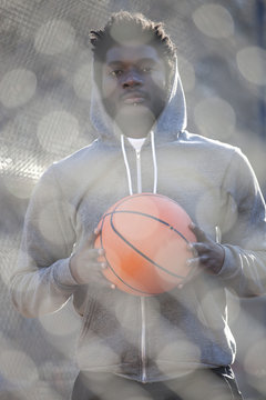 A hip young man holding a basketball and standing on an outdoor basketball court