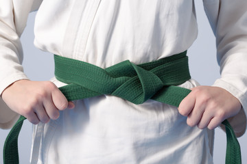 Handen die de groene band aanhalen van een tiener gekleed in kimono voor vechtsporten