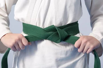 Foto auf Alu-Dibond Kampfkunst Hands tightening green belt on a teenage dressed in kimono for martial arts
