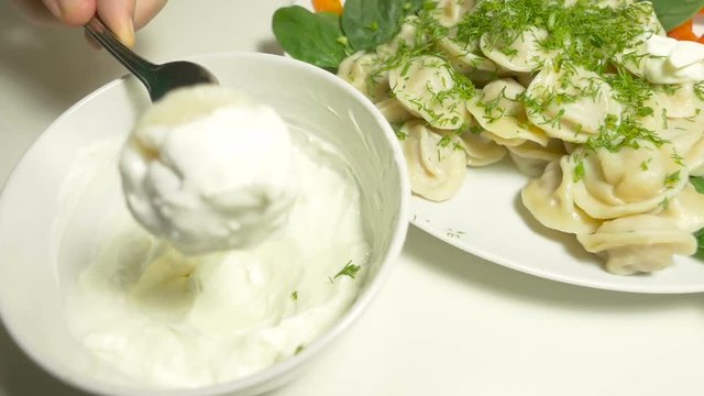 A hand impales meet dumpling with a fork   and dips in a sour cream