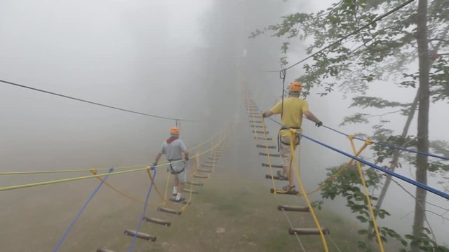 People climbing up the rope ladders in the entertainment park in the forest on a misty or foggy day.  Extreme sports concept.