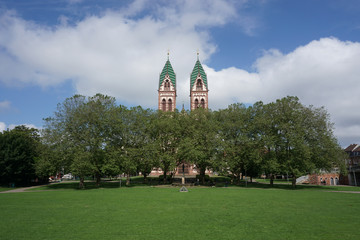 Türme der Herz-Jesu-Kirche in Freiburg mit Bäumen und Wiese im Vordergrund