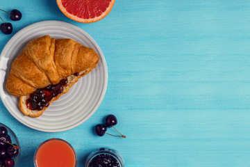 Breakfast with croissant, jam, fruit and juice.
