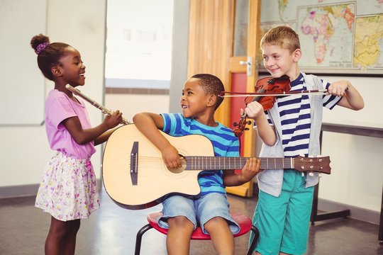 Smiling kids playing guitar, violin, flute in classroom