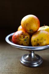 Bad rotten apples on a silver pedestal dish against black