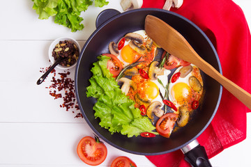Fried eggs in pan with salad, tomato, pepper and spice on wthe table