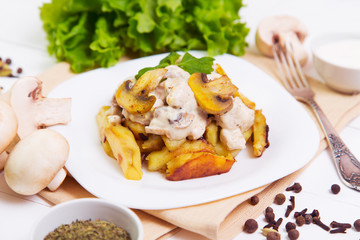 Fried potatoes with gravy of mushrooms in a plate on wooden background