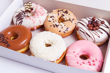 Colored delicious donuts with glaze in a box on a white wooden background
