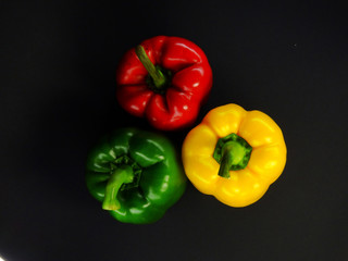 3 bright peppers on a black background: red, green, yellow