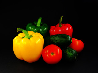 composition still life on a black background three peppers, two cucumbers and two tomatoes