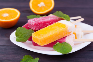 Colored popsicles on a plate with melissa on the wooden background