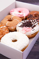 Colorful delicious donuts with glaze and sprinkles in a box on a dark wooden table. Top view with copy space
