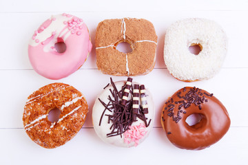 Colorful delicious donuts with chocolate, coconut and other sprinkles on a wooden background