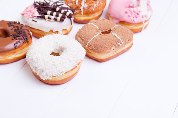 Colored delicious donuts with chocolate, coconut and other sprinkles on a white wooden background