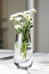 Bouquet of daisies standing in glass vase on white table