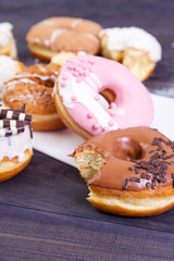 Colorful bitten donuts with crumbs, glaze and sprinkles on a dark wooden background