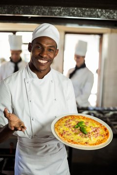 Portrait of smiling chef showing pizza 