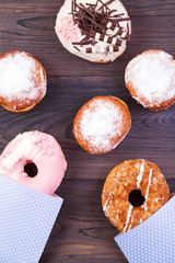 Colofrul donuts and German berliners with glaze and sprinkles on a dark wooden background. Top view