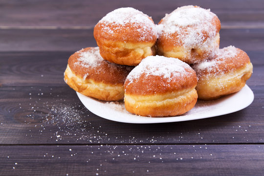 German donuts - berlGerman donuts - berliner with icing sugar on plate on a dark wooden backgroundiner
