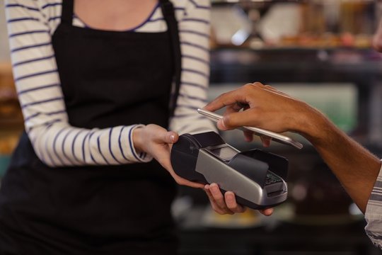 Hand of customer paying by bank card reader with his smartphone