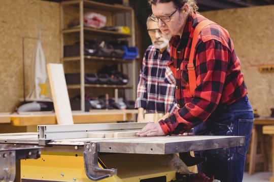 Focused duo of carpenter cutting a wood plank