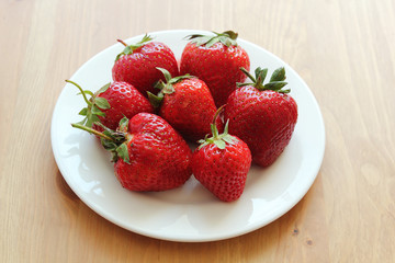 Strawberries in white plate on wooden brown desk.