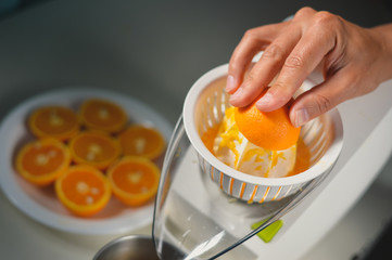 Hand making orange juice with juicer on kitchen table background. Closeup