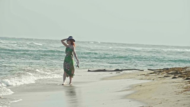 Young woman In long Dress hold a hat and Walking along the sea, slow-motion