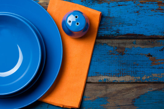 Empty blue plates and orange napkin on wooden background - Powered by Adobe