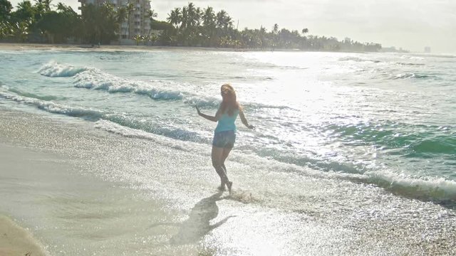 Young woman with long red hair in shorts pants play with waves running, feeling the sea, seascape, beach of Dominican Republic